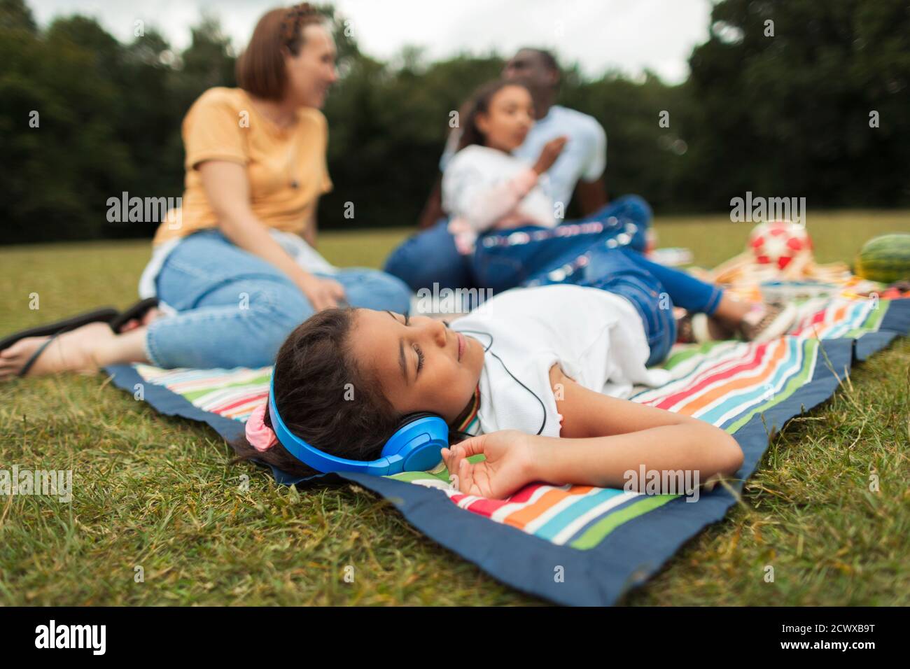 Ragazza con le cuffie che si rilassa e ascolta la musica durante il picnic coperta Foto Stock