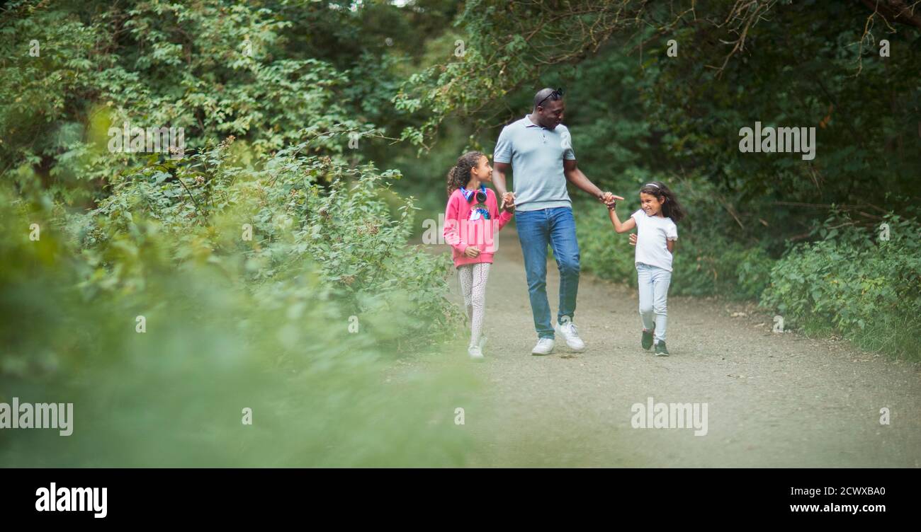 Padre e figlie che tengono le mani sul sentiero nel parco Foto Stock