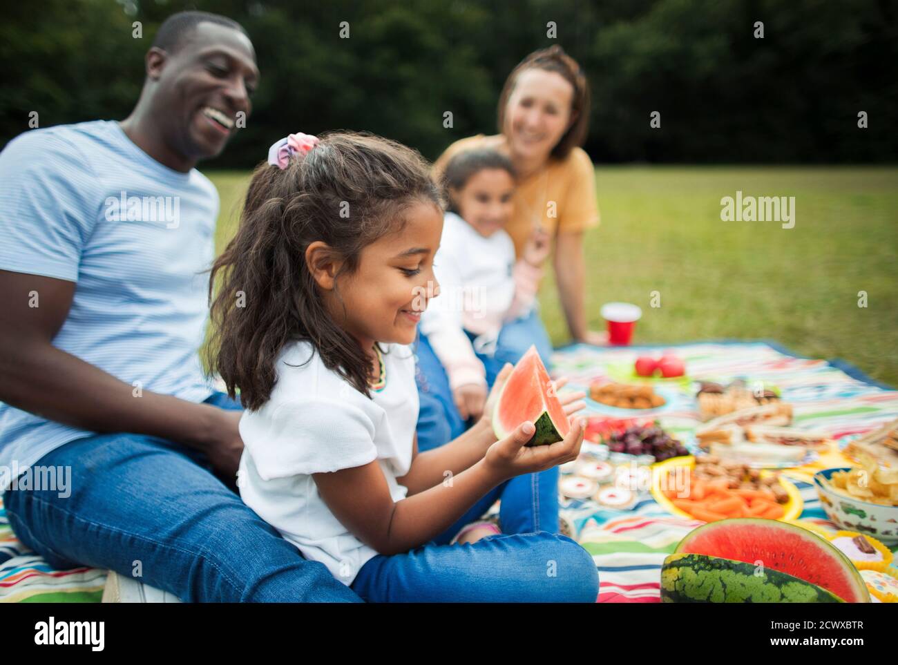 Ragazza felice mangiare cocomero con la famiglia su coperta da picnic dentro parcheggio Foto Stock