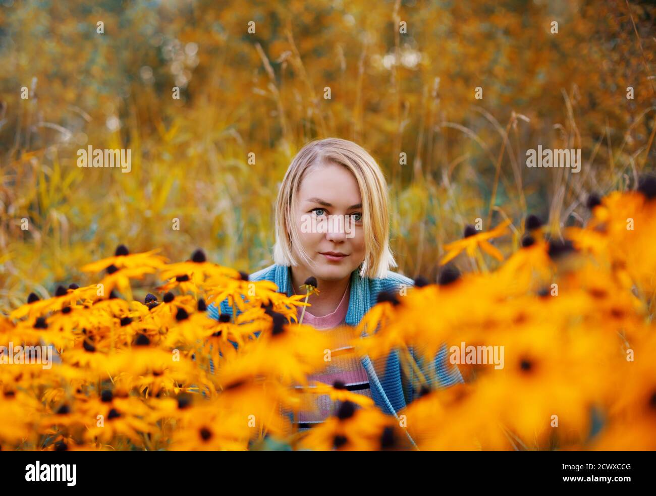 Bella donna bionda seduta al prato di fiori nella foresta d'autunno. Ritratto colorato all'aperto nella stagione autunnale Foto Stock