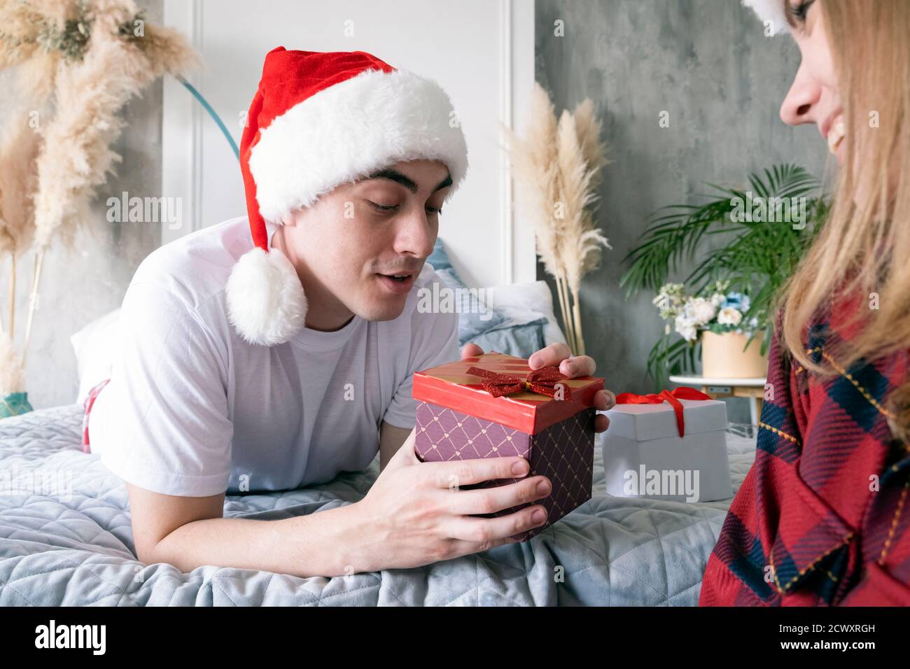 Natale, vacanze, inverno e concetto di gente. Felice coppia con regalo di natale a casa indossando cappelli santa. Foto Stock