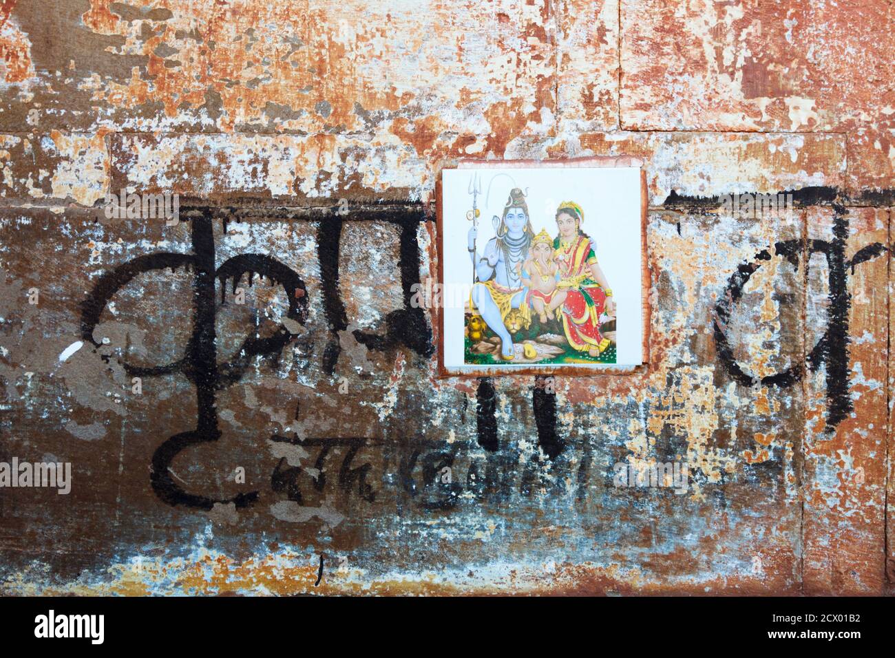 Varanasi, Uttar Pradesh, India : primo piano di un muro intemperato con la scritta Devanagari e una piastrella raffigurante gli dei Shiva, Parvati e Ganesh. Foto Stock