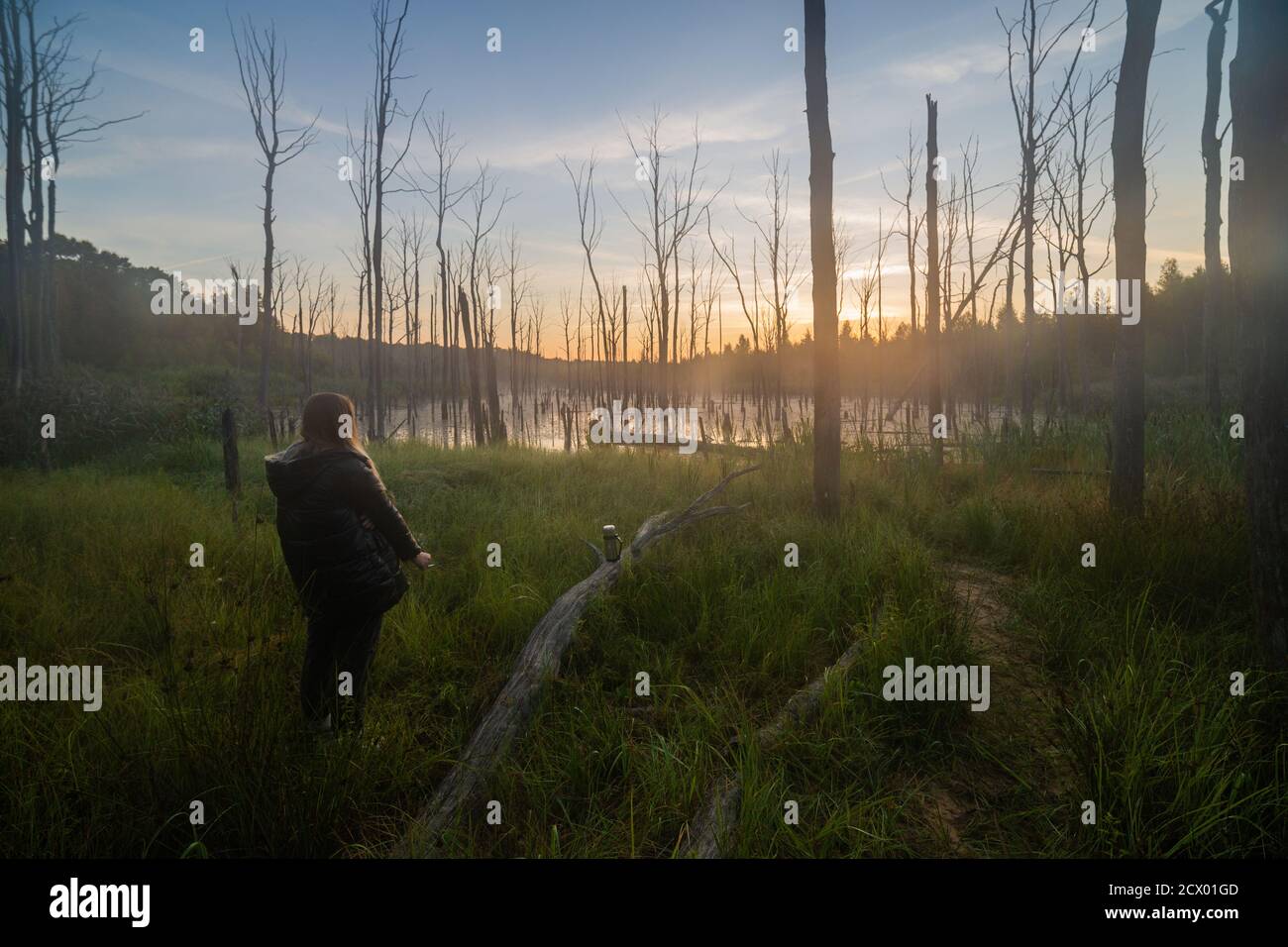 giovane bionda caucasica donna che fuma sul bordo della mattina palude estiva con tronco di albero grigio asciutto - ampia da sogno angolo di ripresa Foto Stock