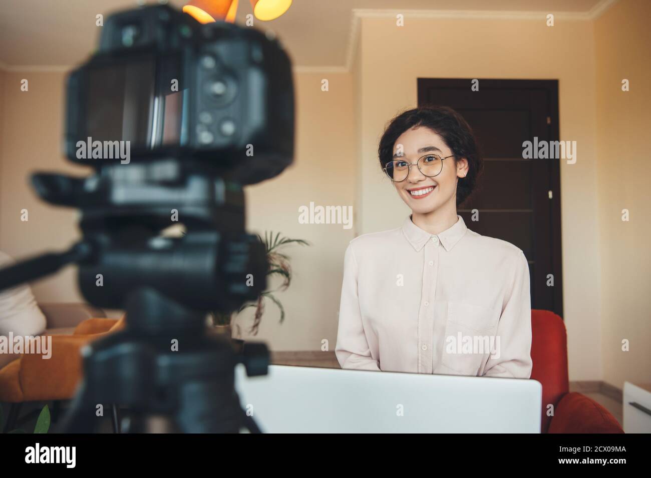 Signora brunette affascinante sta avendo una riunione in linea usando un fotocamera e computer portatile indossando abiti da formalwear Foto Stock