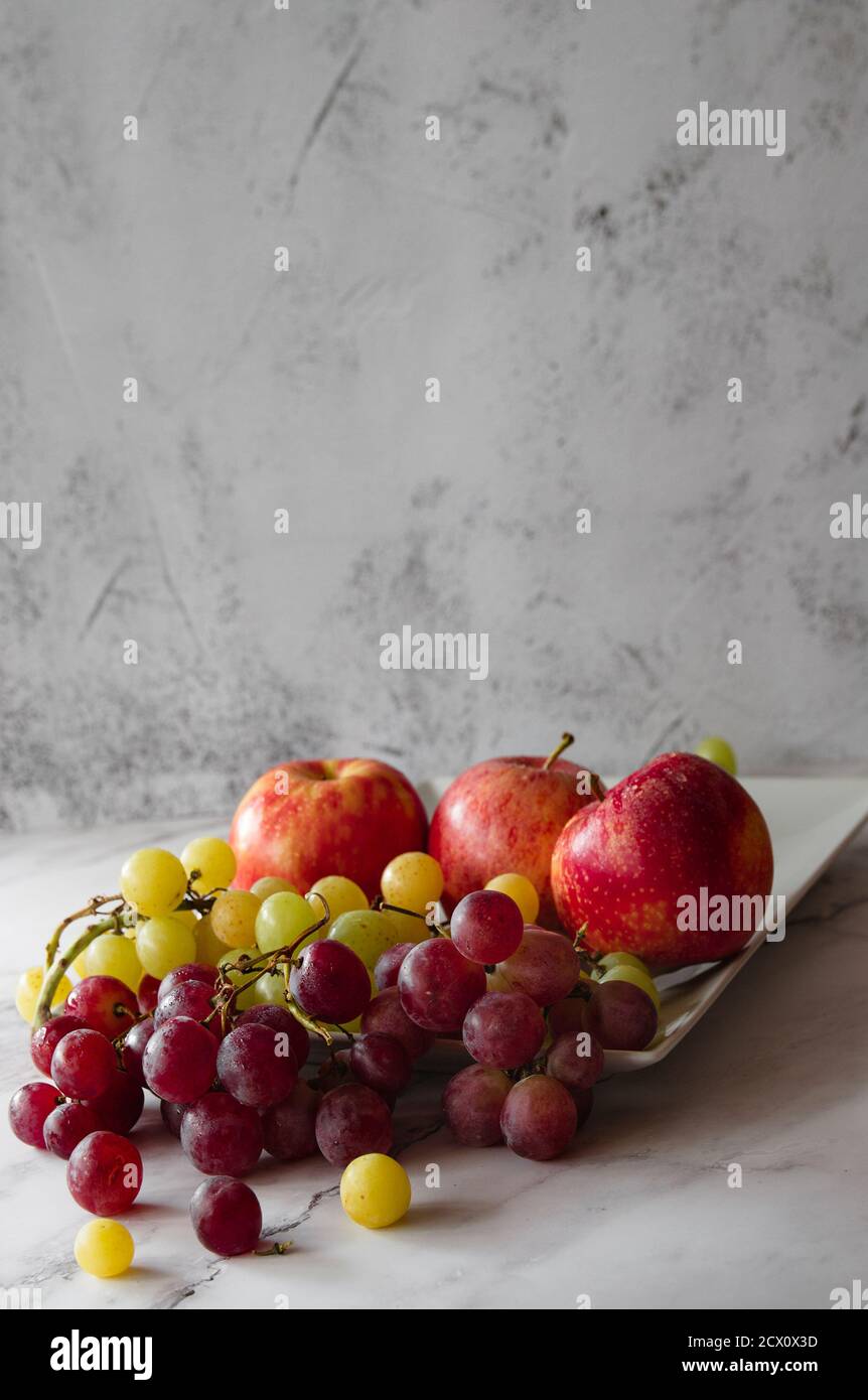 Tavolo in marmo bianco con diverse mele rosse e uve viola e gialle. Frutti tipici autunnali Foto Stock