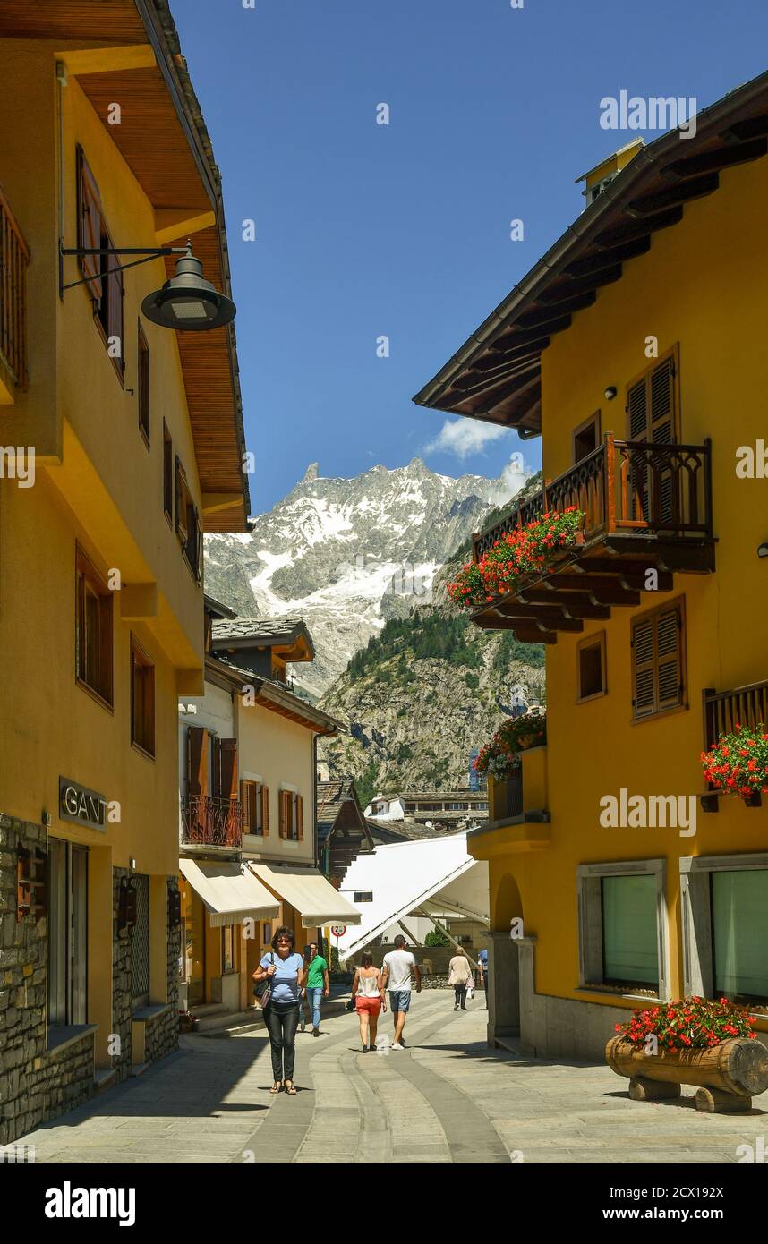 Scorci della famosa città di montagna con persone che camminano nella principale strada pedonale e il massiccio del Monte Bianco in estate, Courmayeur, Aosta, Italia Foto Stock