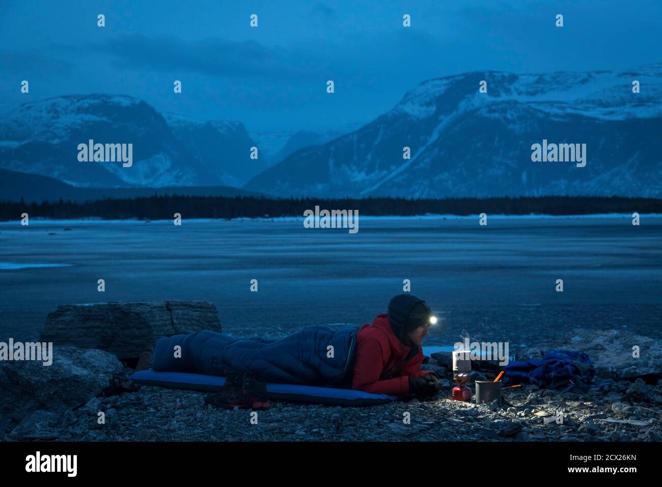 Escursionista maschile preparare il cibo mentre si sdraia in sacco a pelo sopra montagna al tramonto Foto Stock