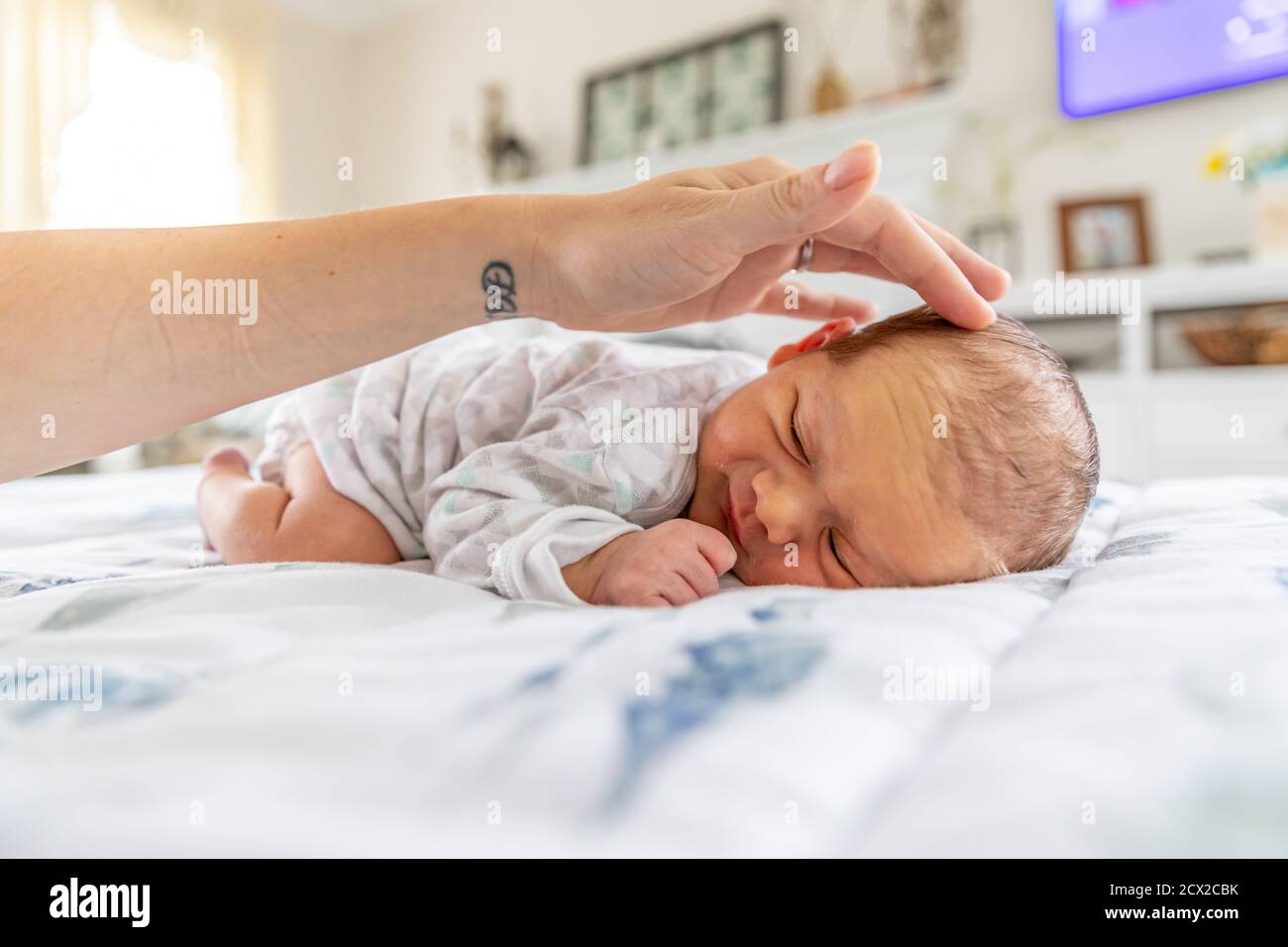 Sorridi bambino neonato che posa sullo stomaco mentre la madre tocca delicatamente la testa. Foto Stock