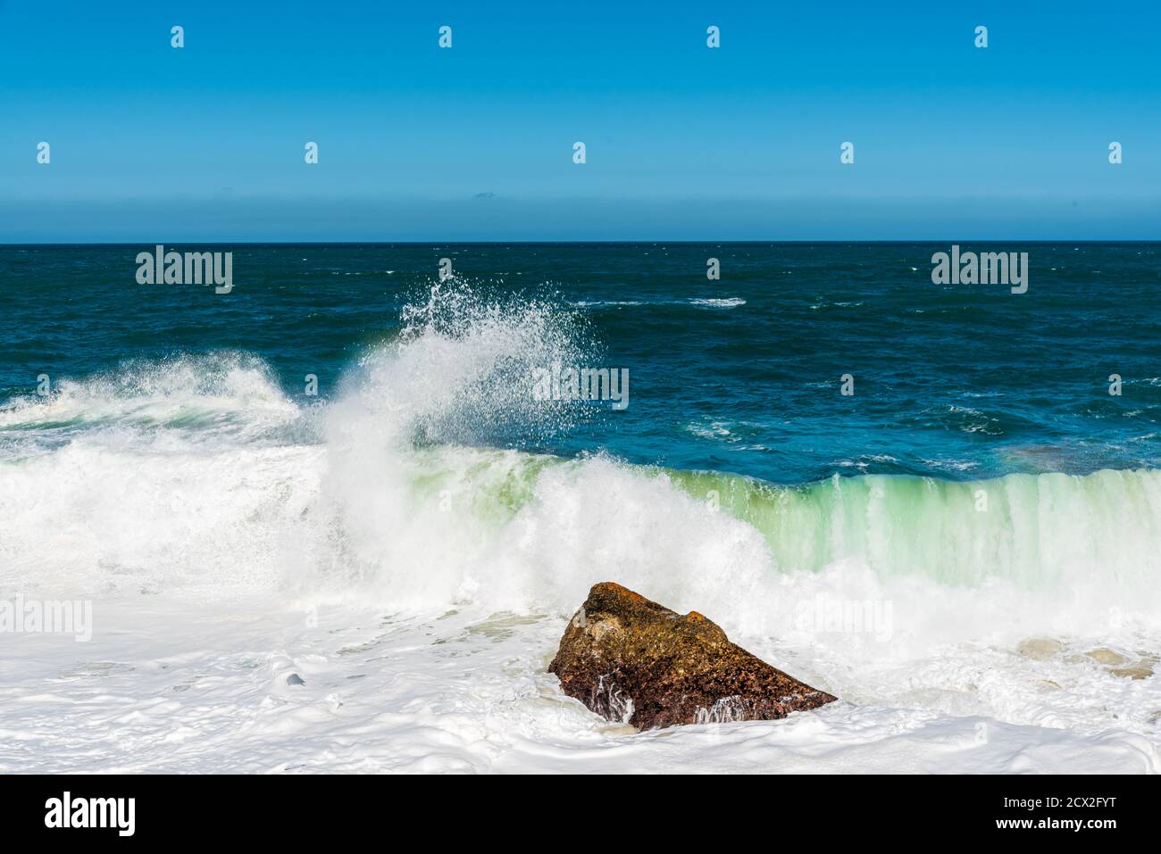 L'onda dell'oceano scorre verso la roccia sulla spiaggia Foto Stock