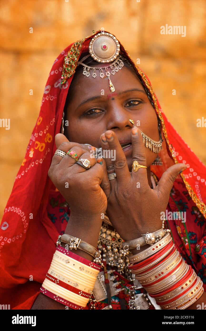 Ritratto di una donna Rajasthani in abito Rajasthani distintivo e gioielli giocando una arpa bocca, Jaisalmer, India. Questa immagine contiene materiale culturalmente rilevante: 1. Rajasthani gioielli etnici. 2. Un sari è un indumento femminile dell'Asia del Sud che consiste di un telo che varia da 4 a 8 metri di lunghezza e 60cm a 1.20m di larghezza che è tipicamente avvolto intorno alla vita, con un'estremità drappeggiato sopra la spalla, che brandisce il midriff. Il sari è solitamente indossato sopra un petticoat. I sari sono associati alla grazia ed è ampiamente considerato come un simbolo della cultura indiana. Foto Stock