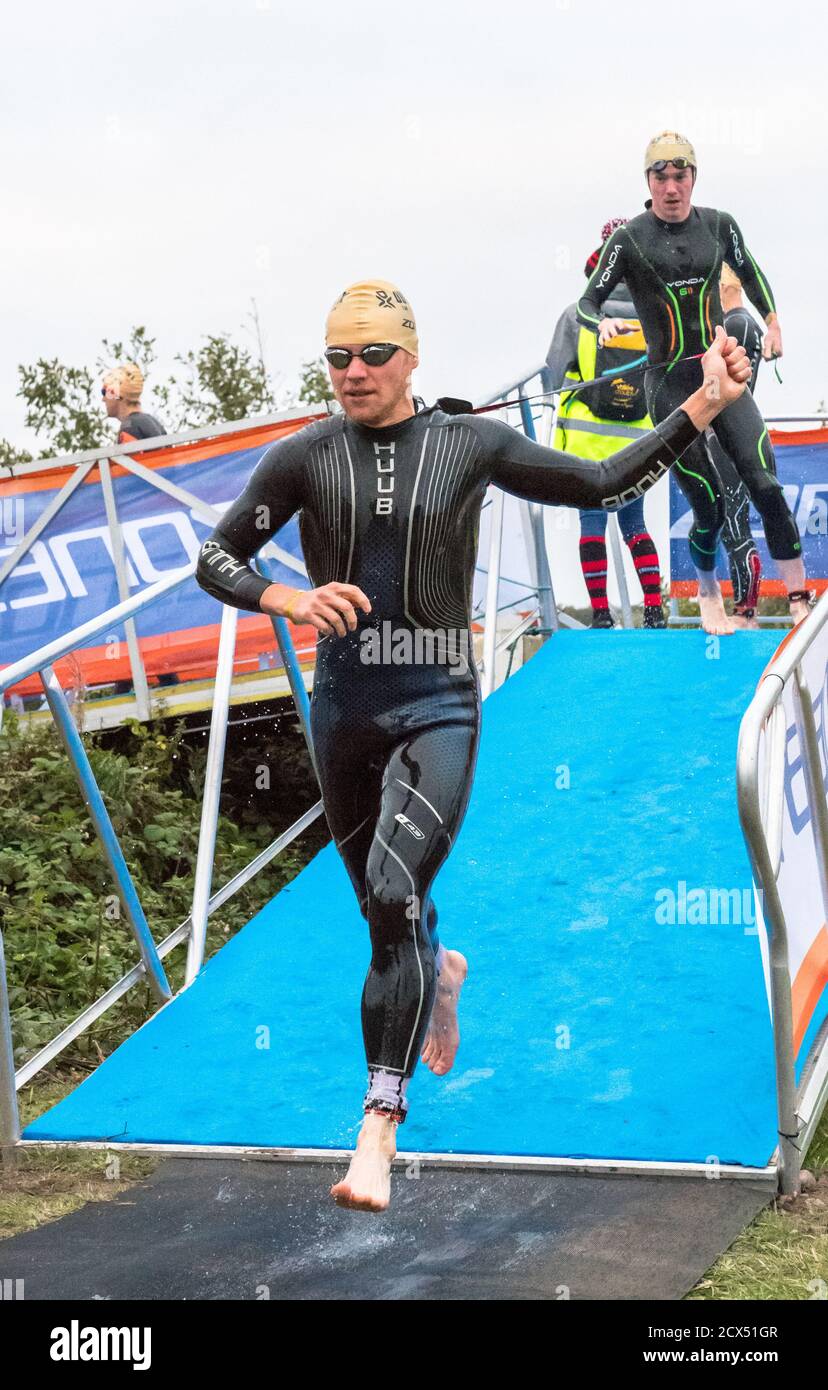 Gli atleti professionisti Elite maschili terminano il loro primo evento, nuotare, all'ultimo triathlon dell'anno con le loro tute umide. Foto Stock Gli atleti professionisti Elite maschili terminano il loro primo evento, nuotare, all'ultimo triathlon dell'anno con le loro tute umide. Foto Stock