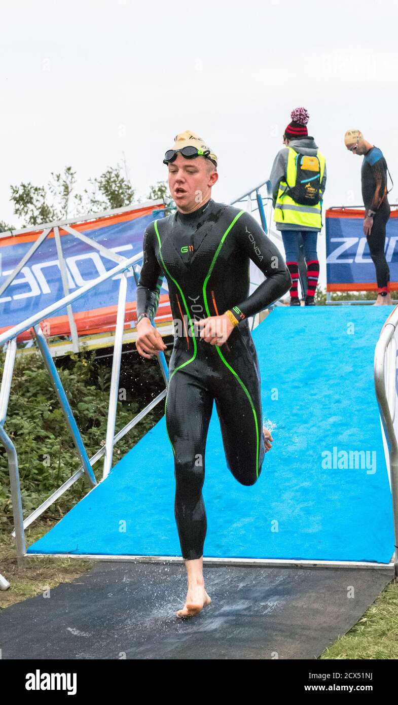 Gli atleti professionisti Elite maschili terminano il loro primo evento, nuotare, all'ultimo triathlon dell'anno con le loro tute umide. Foto Stock