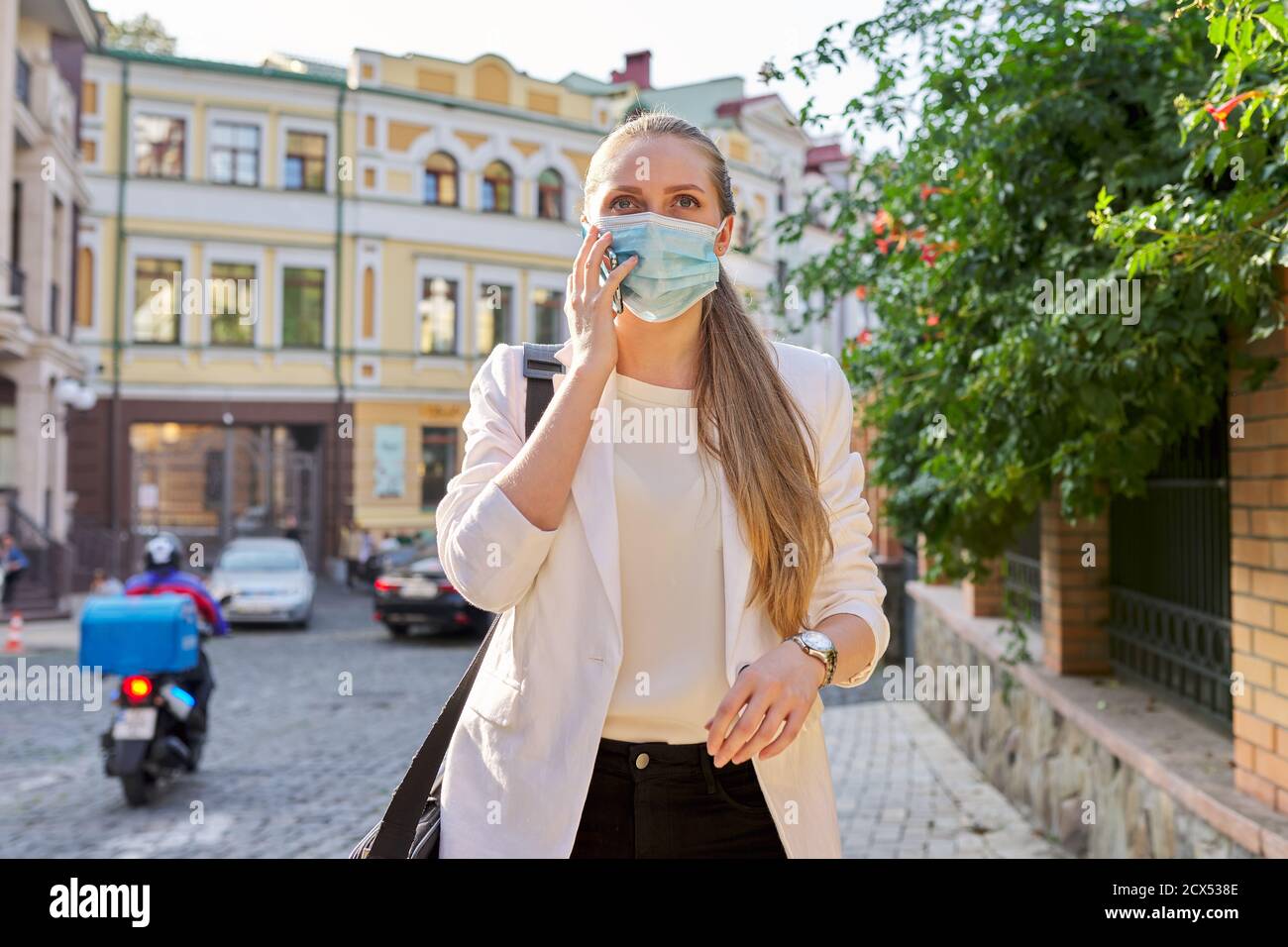 Ritratto di giovane donna d'affari in una maschera medica di protezione che parla sul cellulare Foto Stock