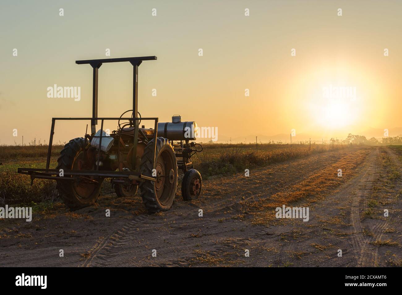 Un vecchio trattore agricolo è inutilizzato, bagnato dalla luce del sole che sorge su una strada sterrata accanto ad un paddock pronto per l'aratura a Mareba, Australia. Foto Stock