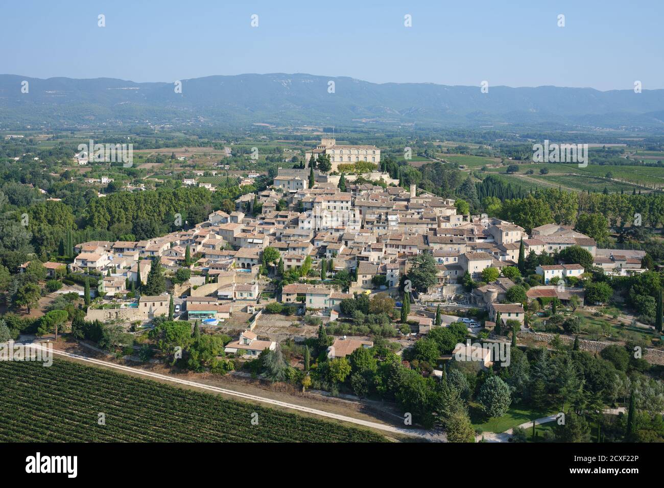 VISTA AEREA. Borgo medievale con il suo castello in cima, che domina i campi agricoli della Valle della Durance. Ansouis, Vaucluse, Francia. Foto Stock