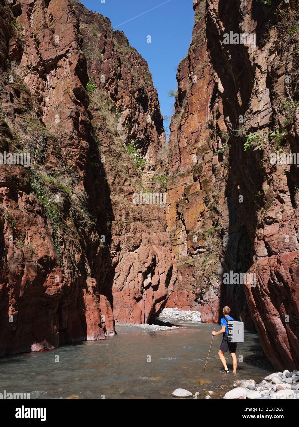 Escursionista che guastano il fiume Var con uno zaino impermeabile in custodia rigida in fondo a un profondo canyon rosso. Daluis Gorge, Guillaumes, Alpes-Maritimes, Francia. Foto Stock