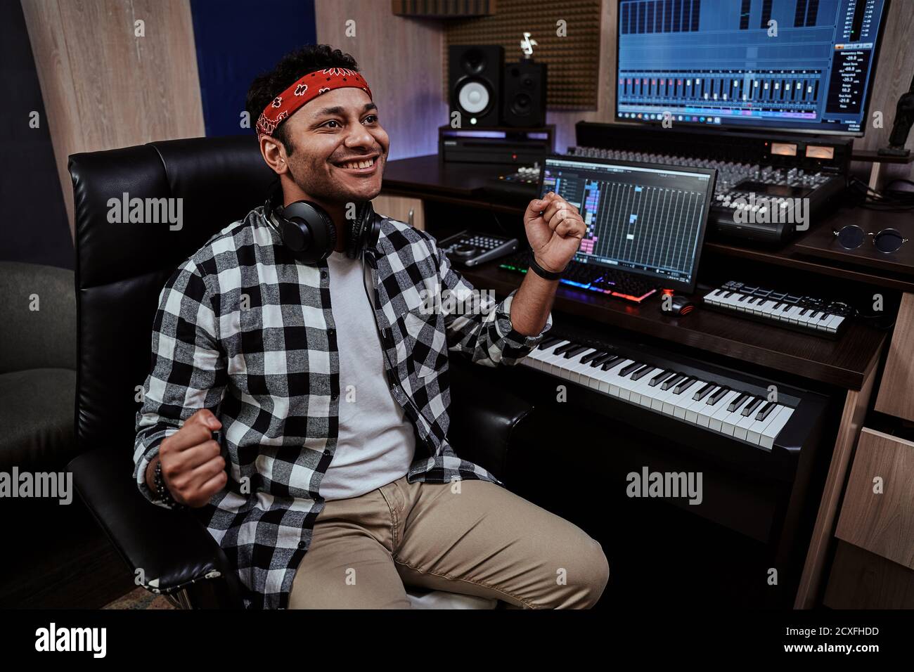 Giovane uomo, artista maschile che guarda felice con due pugni in aria mentre riesce a creare musica, seduto in studio di registrazione Foto Stock