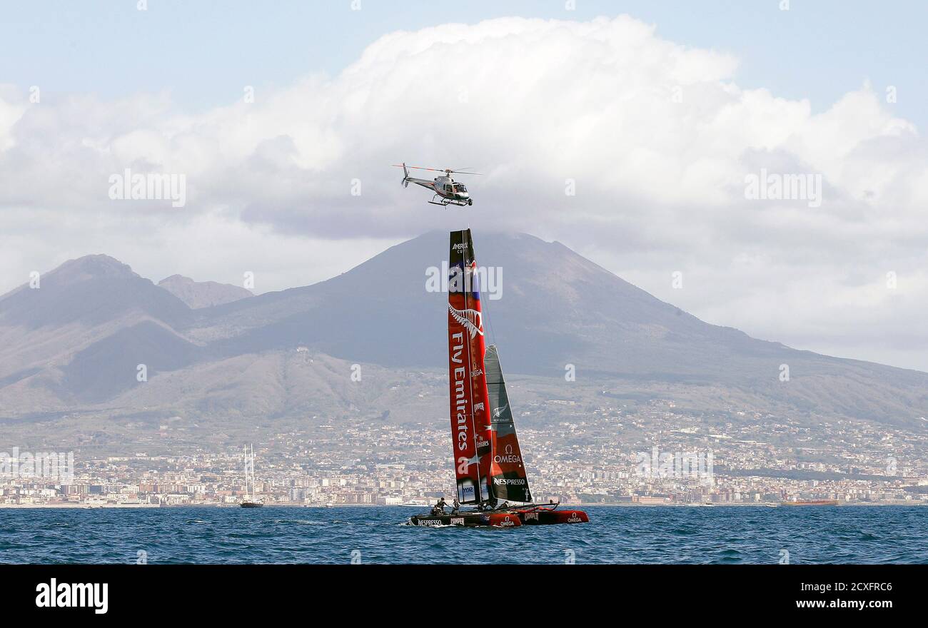 Il team Emirates della Nuova Zelanda gareggia, passando davanti al Vesuvio Vulcan con i loro multiscafi mentre un elicottero sorvola, durante la regata della Coppa del mondo americana a Napoli il 12 aprile 2012. REUTERS/Alessandro Bianchi (ITALIA - Tags: SPORT YACHTING TRASPORTI) Foto Stock