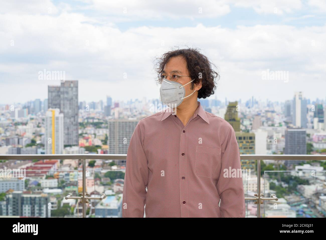 Ritratto di uomo d'affari giapponese pensare con maschera contro vista di la città Foto Stock