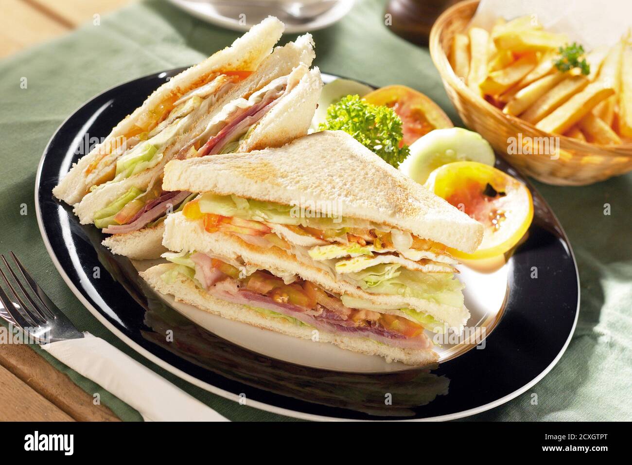 Sandwich con prosciutto, formaggio, pomodori, lattuga, pane tostato e una ciotola di patatine fritte Foto Stock
