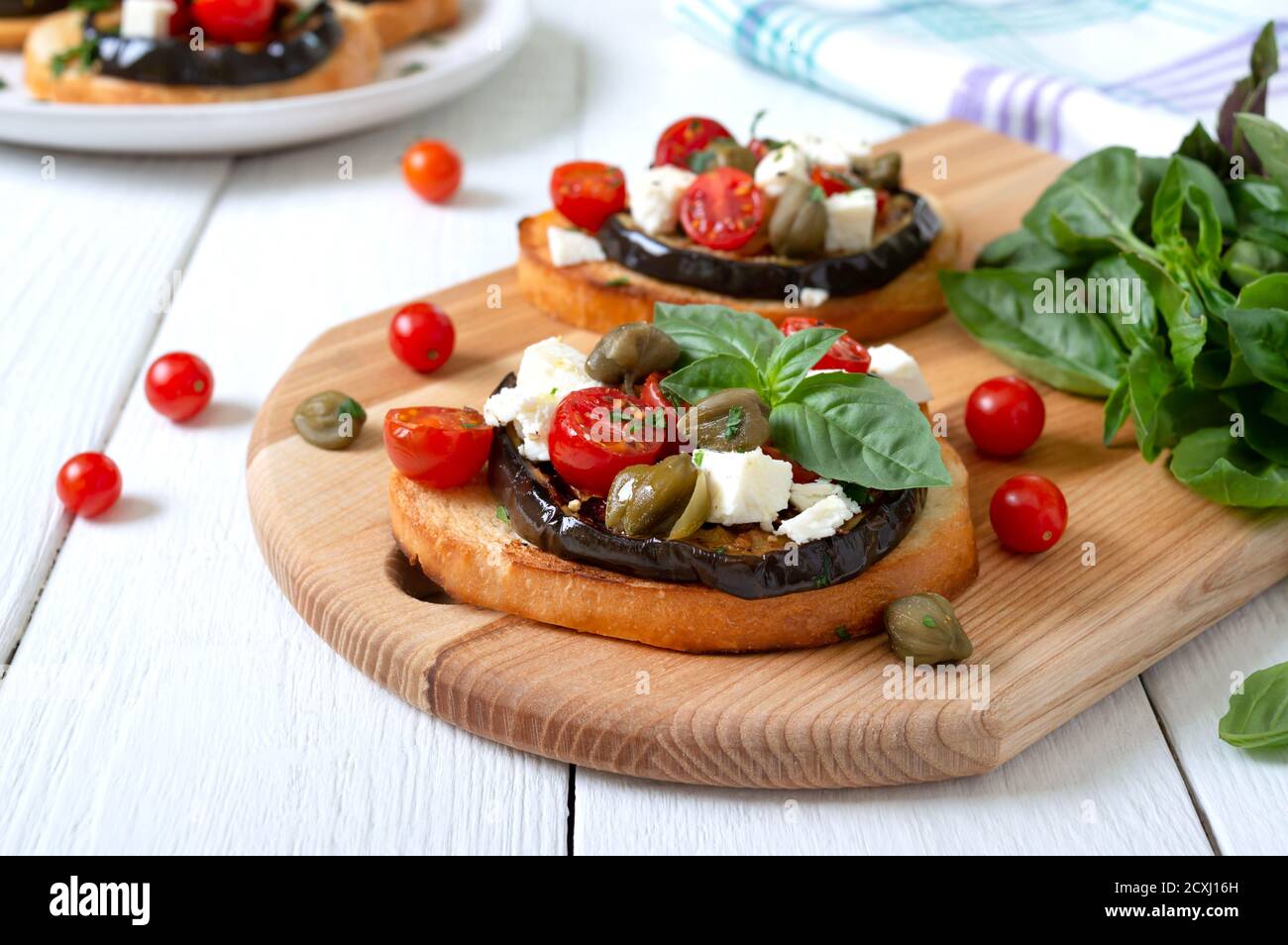 Bruschetta all'aglio con melanzane, feta, pomodori ciliegini, capperi. Utile antipasto vegetariano. Cucina italiana. Foto Stock