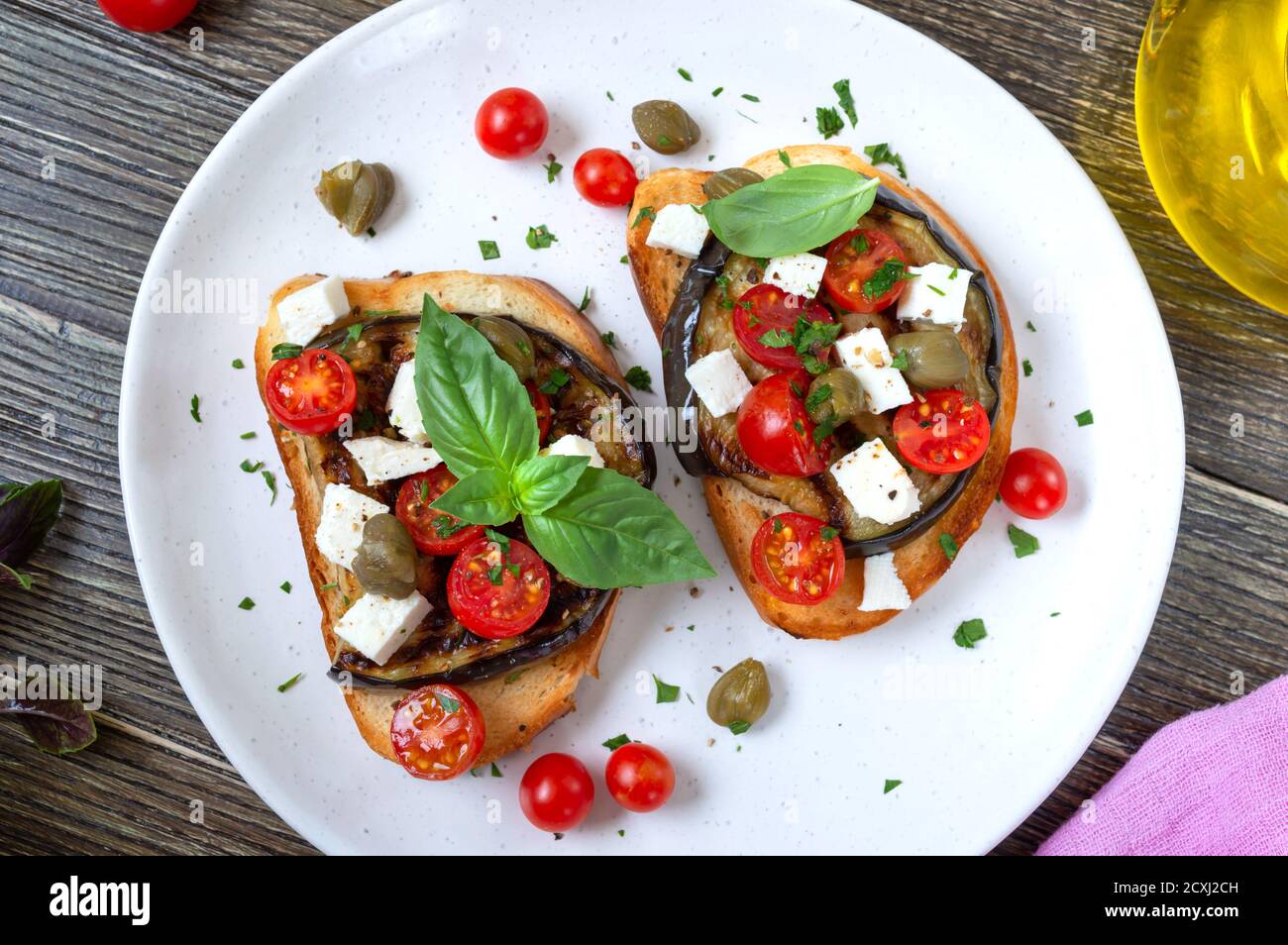 Bruschetta all'aglio con melanzane, feta, pomodori ciliegini, capperi. Utile antipasto vegetariano. Cucina italiana. Foto Stock