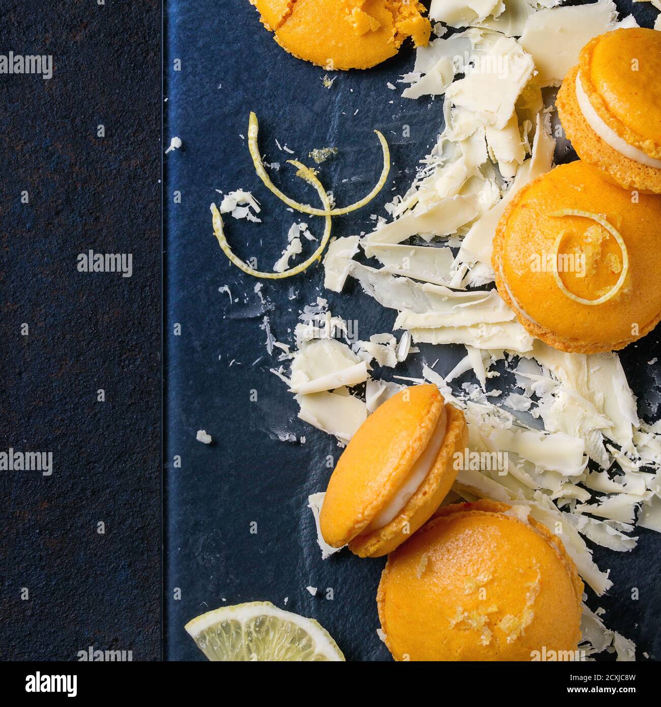 Amaretti interi e spezzati di limone d'arancia fatti in casa con tritato bianco cioccolato e zucchero di agrumi e scorza su tavola di vetro scuro su fondo textural nero gr Foto Stock
