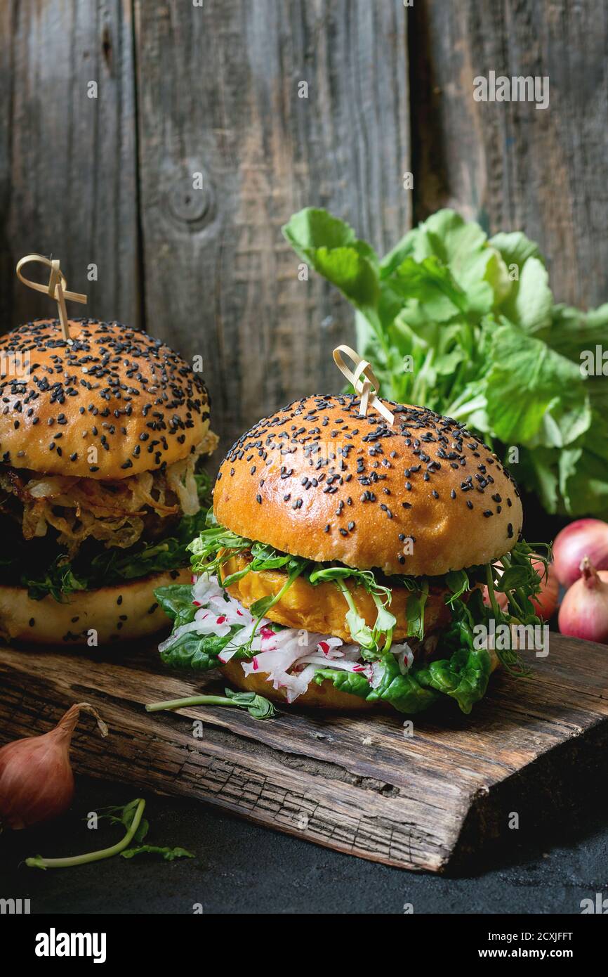Due hamburger di verdure fatti in casa con patate dolci, rafano fresco e germogli di piselli, serviti su trivella di legno su sfondo di legno. Stile rustico scuro Foto Stock