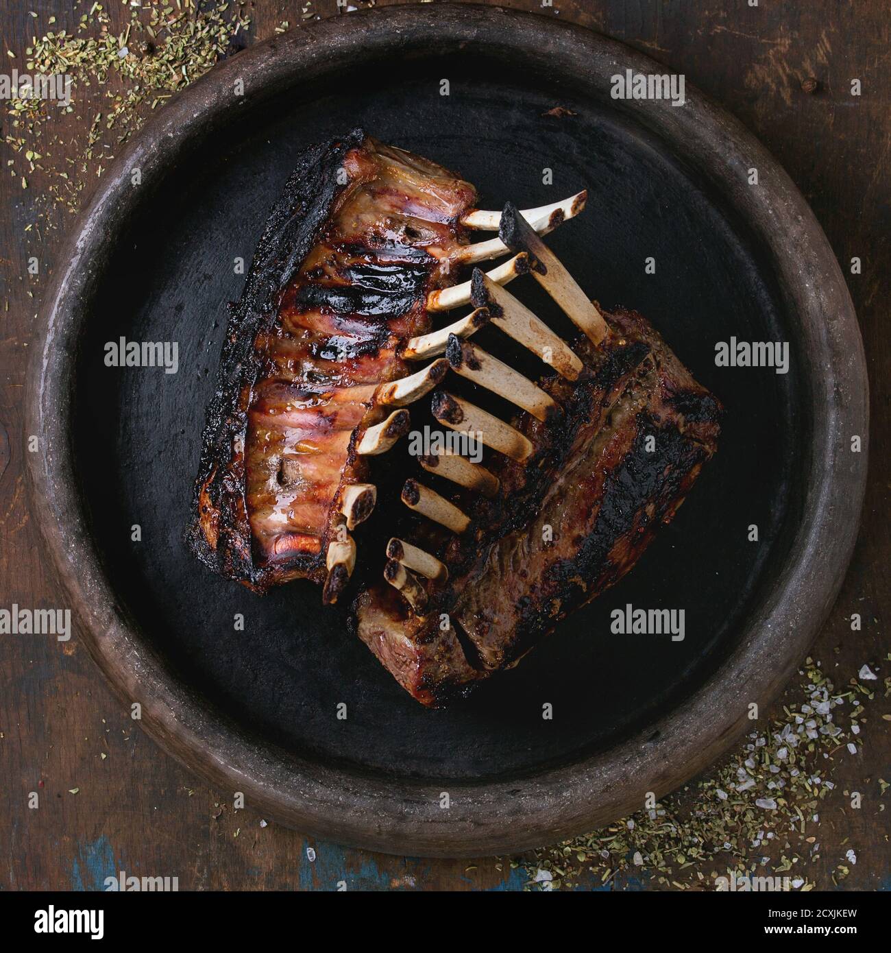 Rack barbecue intero di agnello, servito con condimento su vassoio di argilla su vecchio sfondo di legno. Vista dall'alto. Immagine quadrata Foto Stock