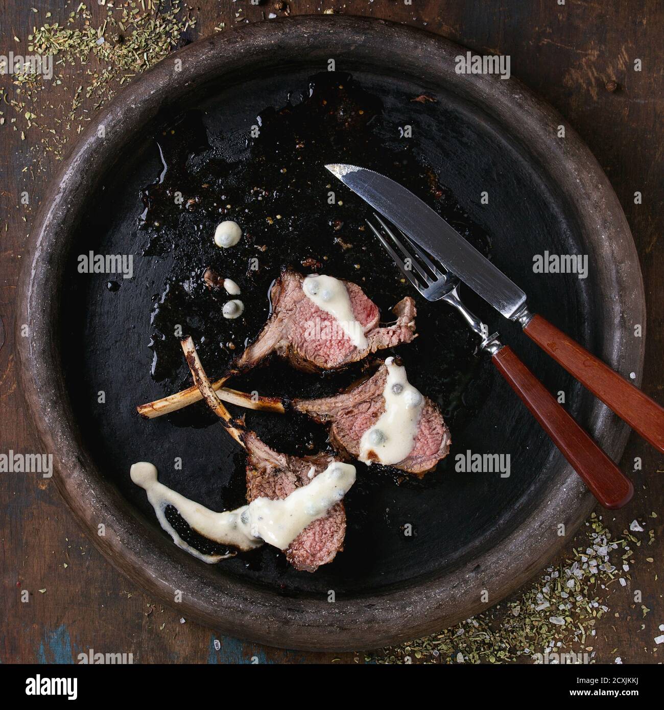 Griglia tritata di agnello alla griglia sotto salsa di pepe, servita con condimento, forchetta e coltello su vassoio di argilla su vecchio sfondo di legno. Vista dall'alto. Quadrato Foto Stock