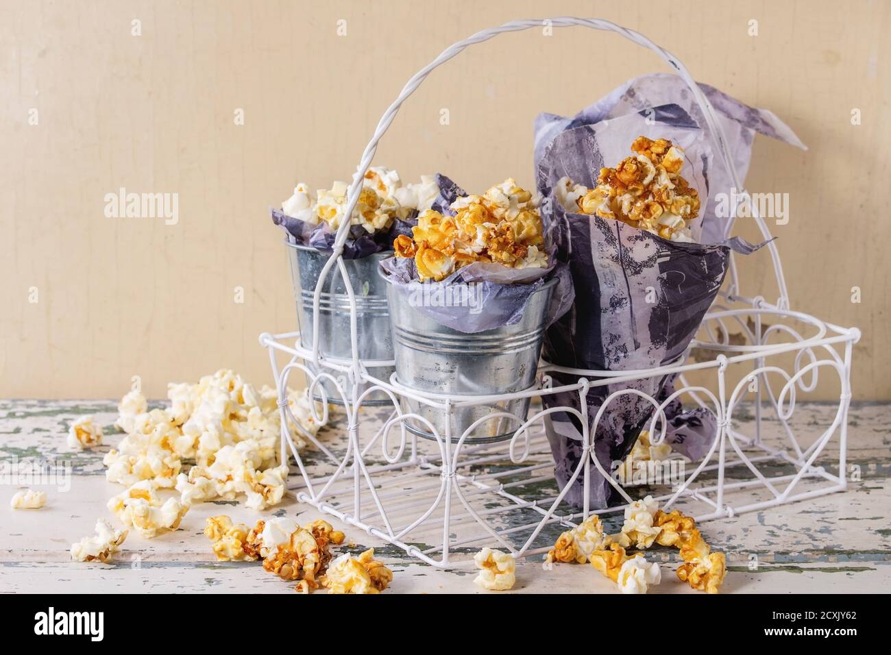 Popcorn dolce preparato salato e caramellato servito in piccoli secchi con carta all'interno e cornet in bianco decorativo in piedi vecchia ba di legno bianco Foto Stock