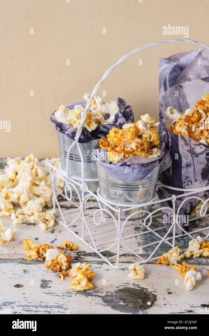 Popcorn dolce preparato salato e caramellato servito in piccoli secchi con carta all'interno e cornet in bianco decorativo in piedi vecchia ba di legno bianco Foto Stock