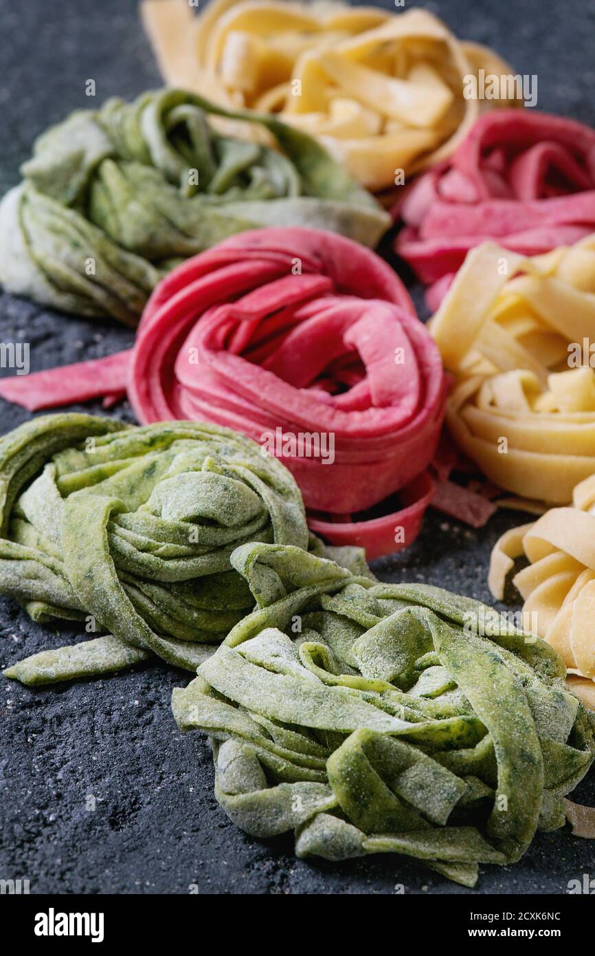 Varietà di tagliatelle di pasta fresca cruda fatte in casa, tagliatelle spinaci verdi, barbabietole rosa e giallo tradizionale su fondo di cemento scuro. Foto Stock