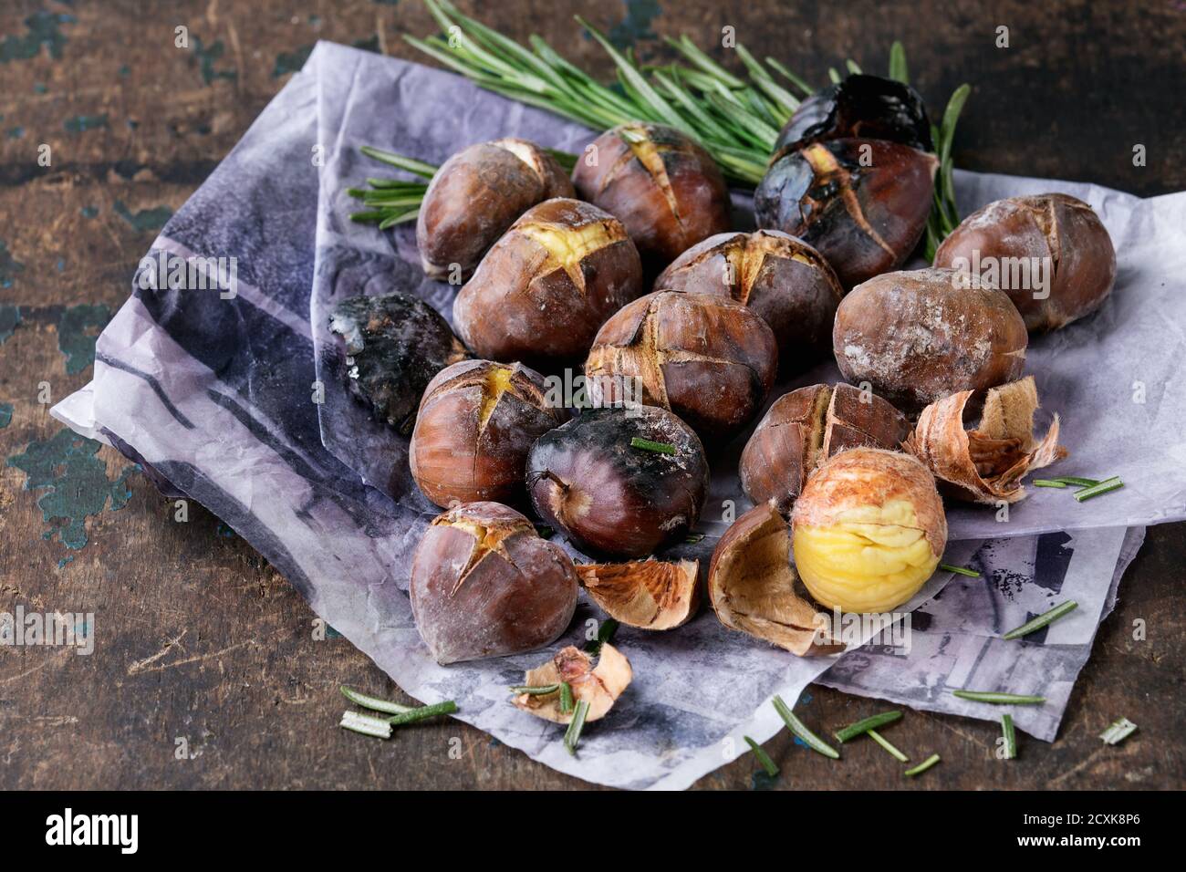 Castagne arrostite nelle ceneri con rosmarino su carta su vecchio fondo di legno di tessitura scura. Primo piano con spazio per il testo. Foto Stock