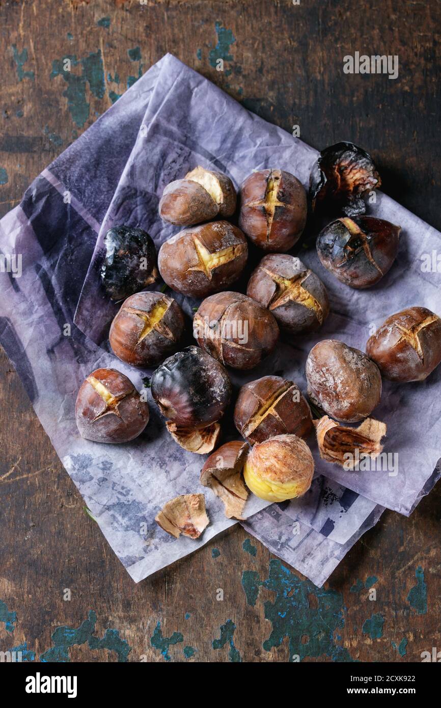 Castagne arrostite nelle ceneri su carta su vecchio fondo di legno di tessitura scura. Vista dall'alto con spazio per il testo. Foto Stock