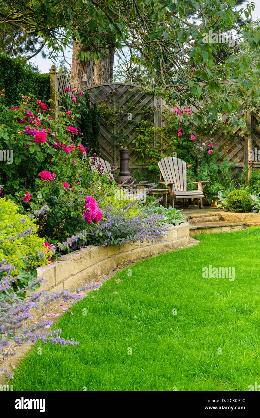 Giardino privato paesaggistico e soleggiato (design contemporaneo, fiori estivi colorati, piante di confine, sedie per mobili da patio, prato) - Yorkshire, Inghilterra, Regno Unito Foto Stock