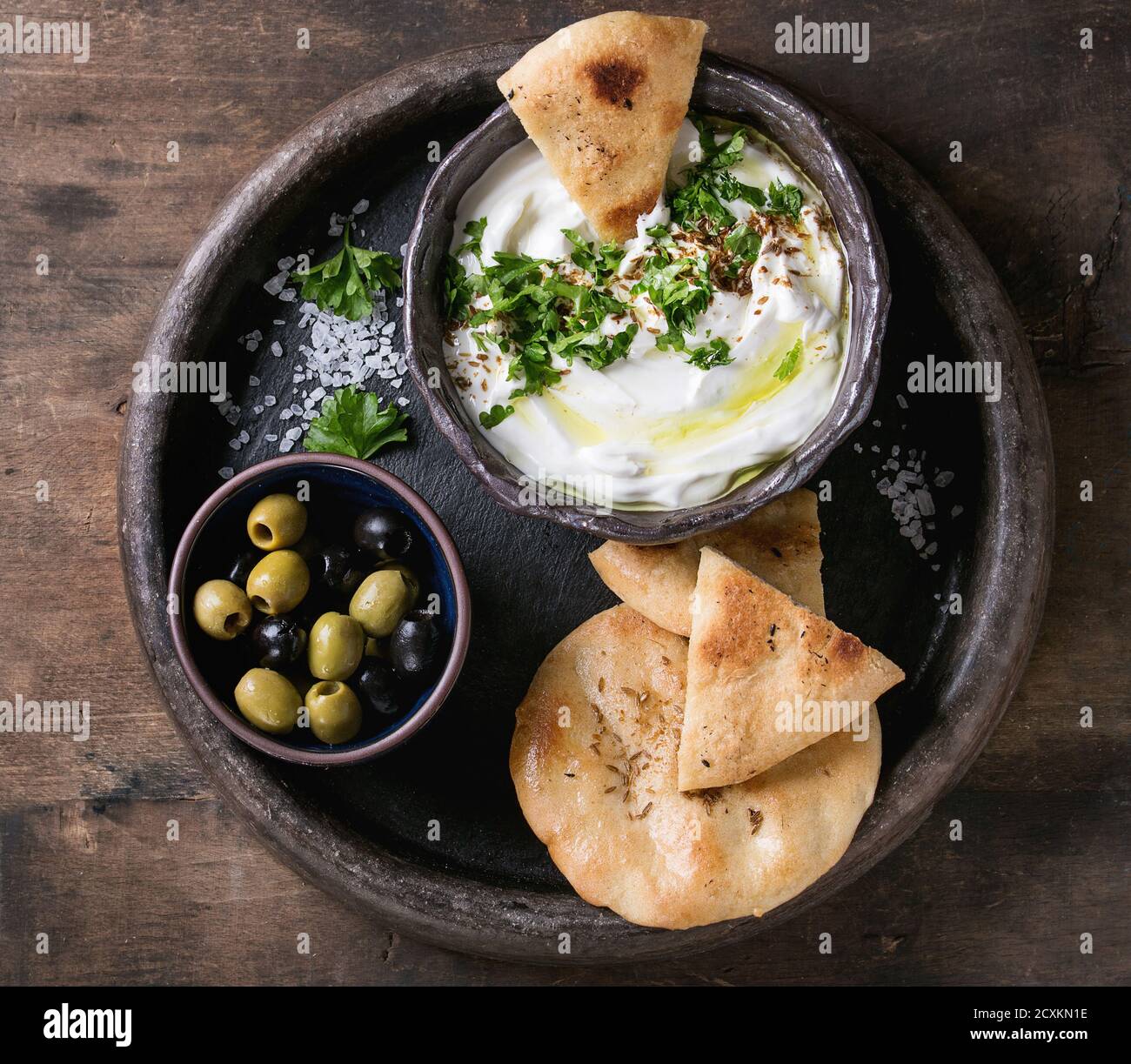 Labneh Middle Eastern libanesi di crema di formaggio dip con olio d'oliva, sale e le erbe aromatiche servita con olive, tradizionale pane pita sulla piastra di terracotta oltre il buio t Foto Stock