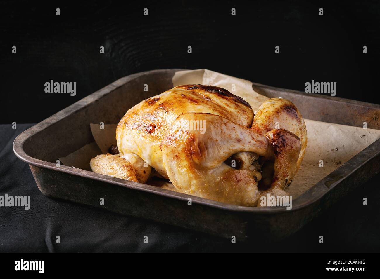 Pollo organico cotto alla griglia su carta di supporto nel vecchio vassoio del forno su sfondo nero di legno bruciato. Vista dall'alto con spazio. Foto Stock