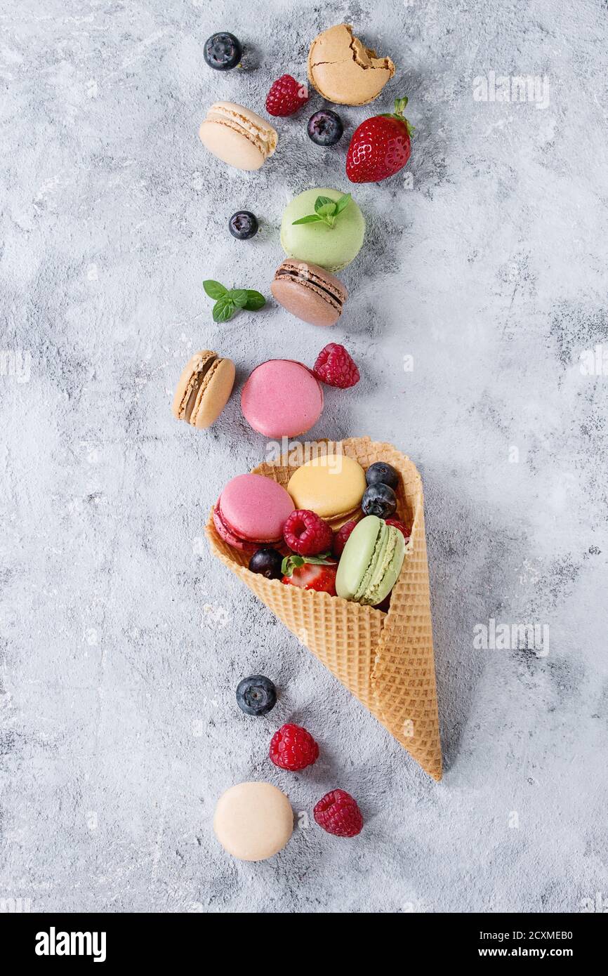 Varietà di colorati macaron dolci francesi con diversi macaron ripieni serviti nel cono del waffle con menta e frutti di bosco freschi trama grigia Foto Stock