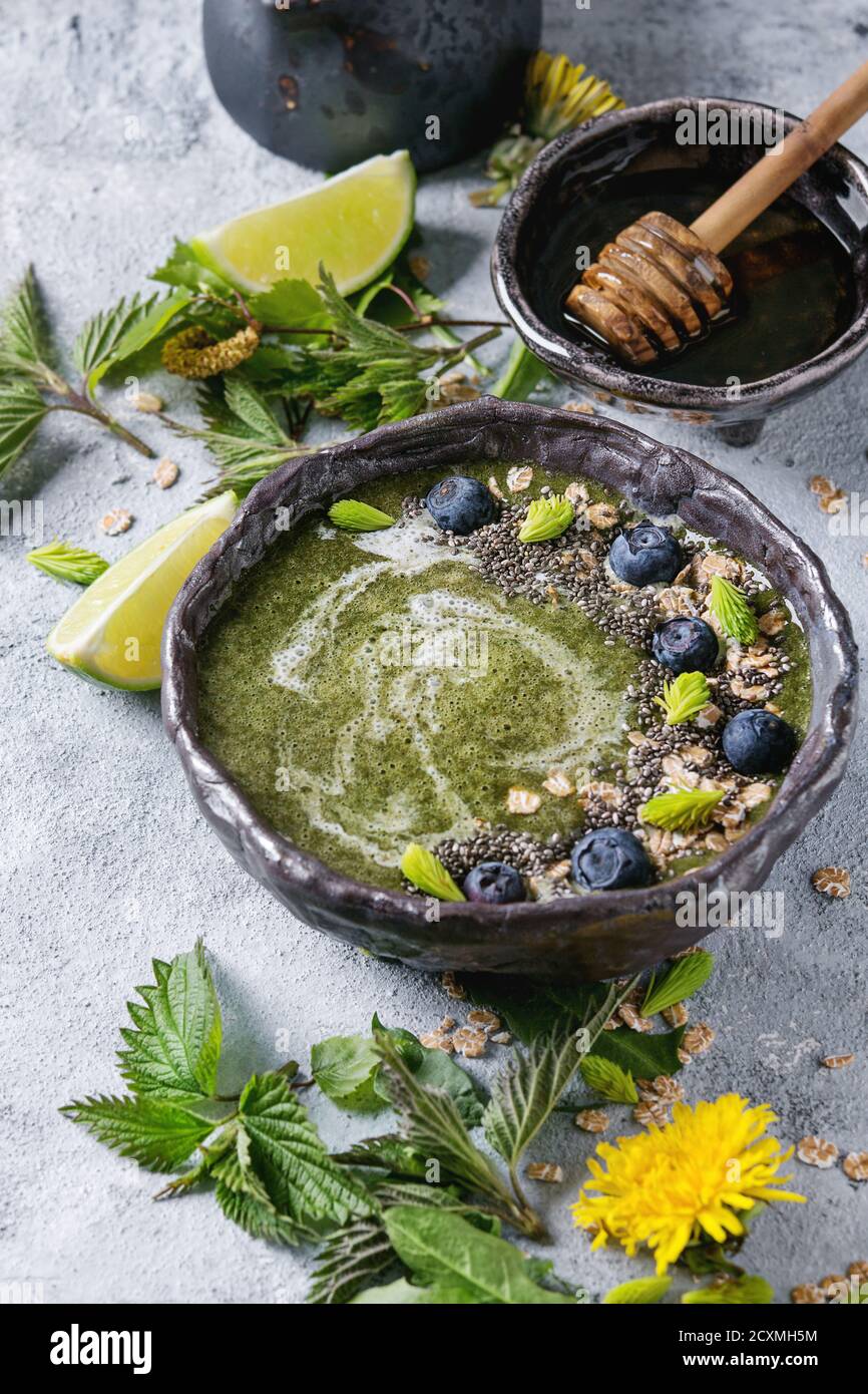 Verde primavera ortica e tarassaco ciotola smoothie servita con calce, fiori gialli, foglie giovani, fiocchi di avena, semi di Chia, mirtilli, la crema di latte e miele o Foto Stock