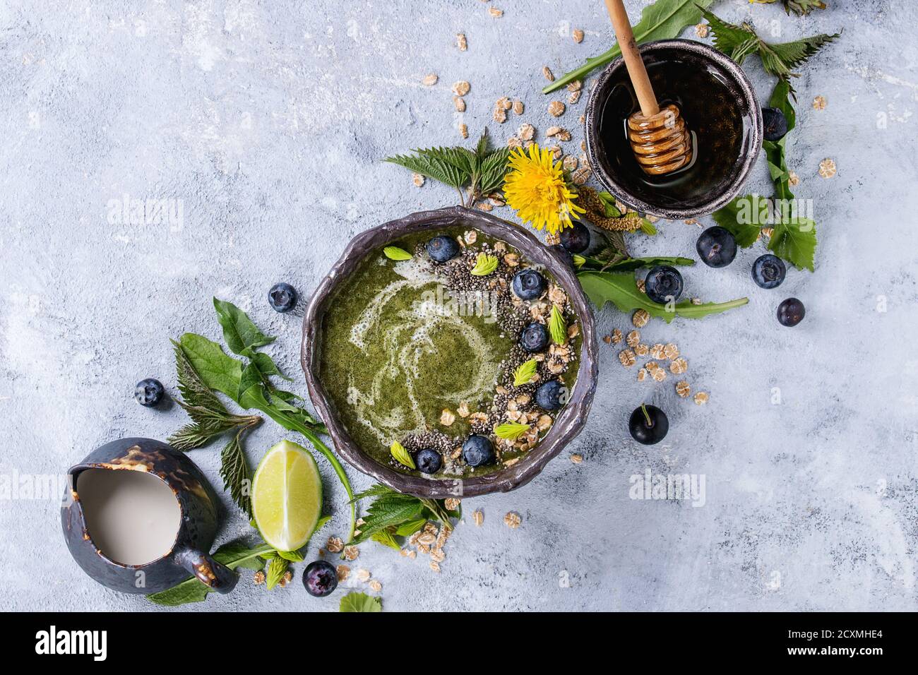Verde primavera ortica e tarassaco ciotola smoothie servita con calce, fiori gialli, foglie giovani, fiocchi di avena, semi di Chia, mirtilli, la crema di latte e miele o Foto Stock