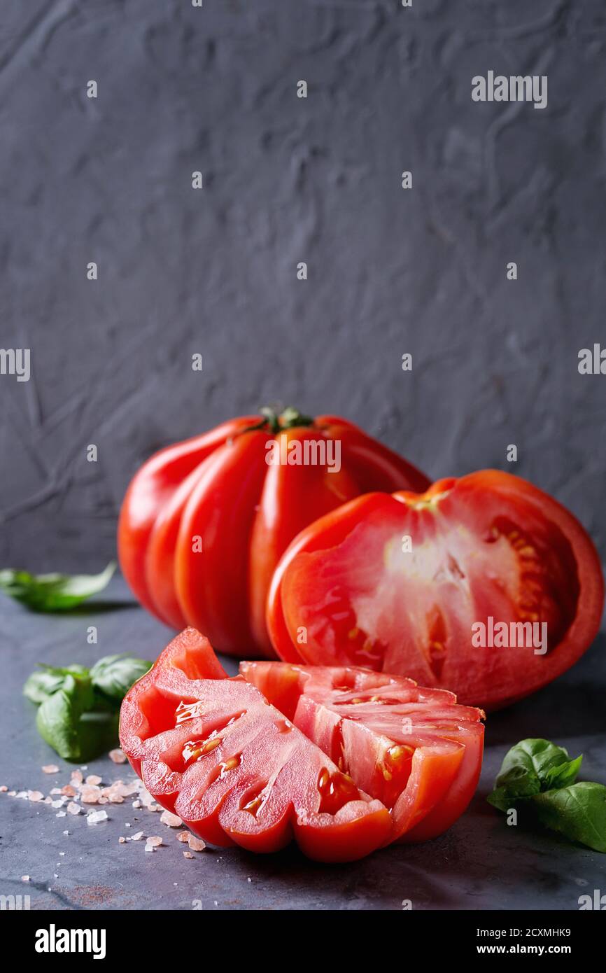 Intero e fette di pomodori organici Coeur De Boeuf. Bistecca di manzo con pomodoro rosa sale e basilico sul blu grigio metallo sfondo texture. Close up con spazio Foto Stock