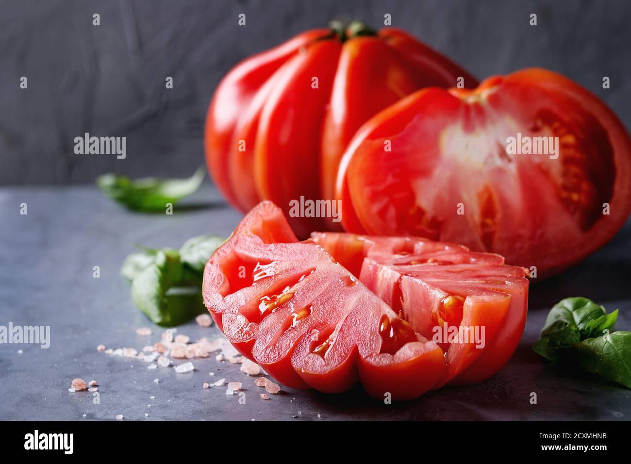 Intero e fette di pomodori organici Coeur De Boeuf. Bistecca di manzo con pomodoro rosa sale e basilico sul blu grigio metallo sfondo texture. Close up con spazio Foto Stock