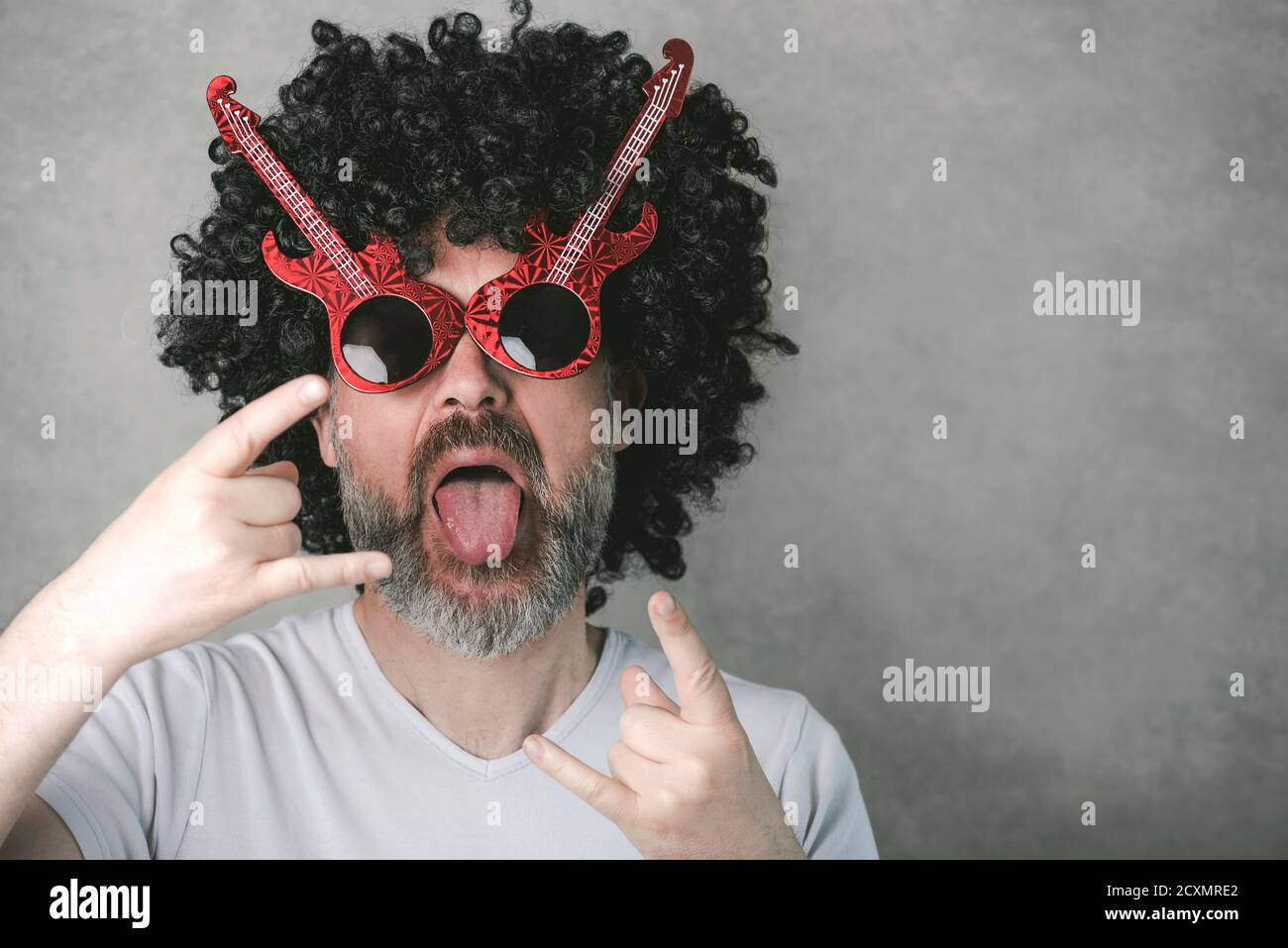 uomo divertente con occhiali da sole che fanno simbolo rock con le mani in su su sfondo grigio Foto Stock