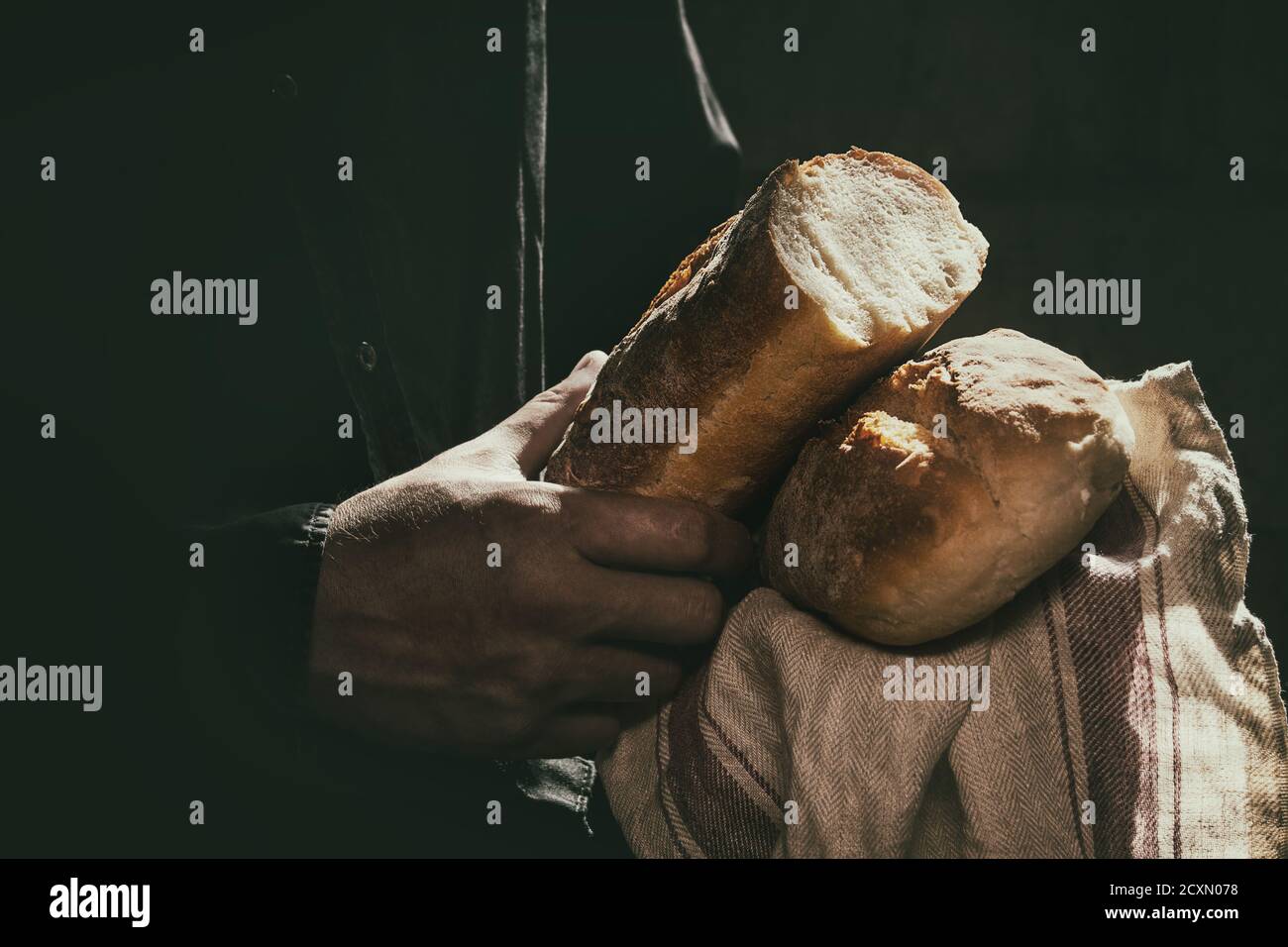 Filone di freschi di forno pane di grano nelle mani dell'uomo nella luce del sole. Giorno rustico luce in camera oscura. Immagine dai toni Foto Stock