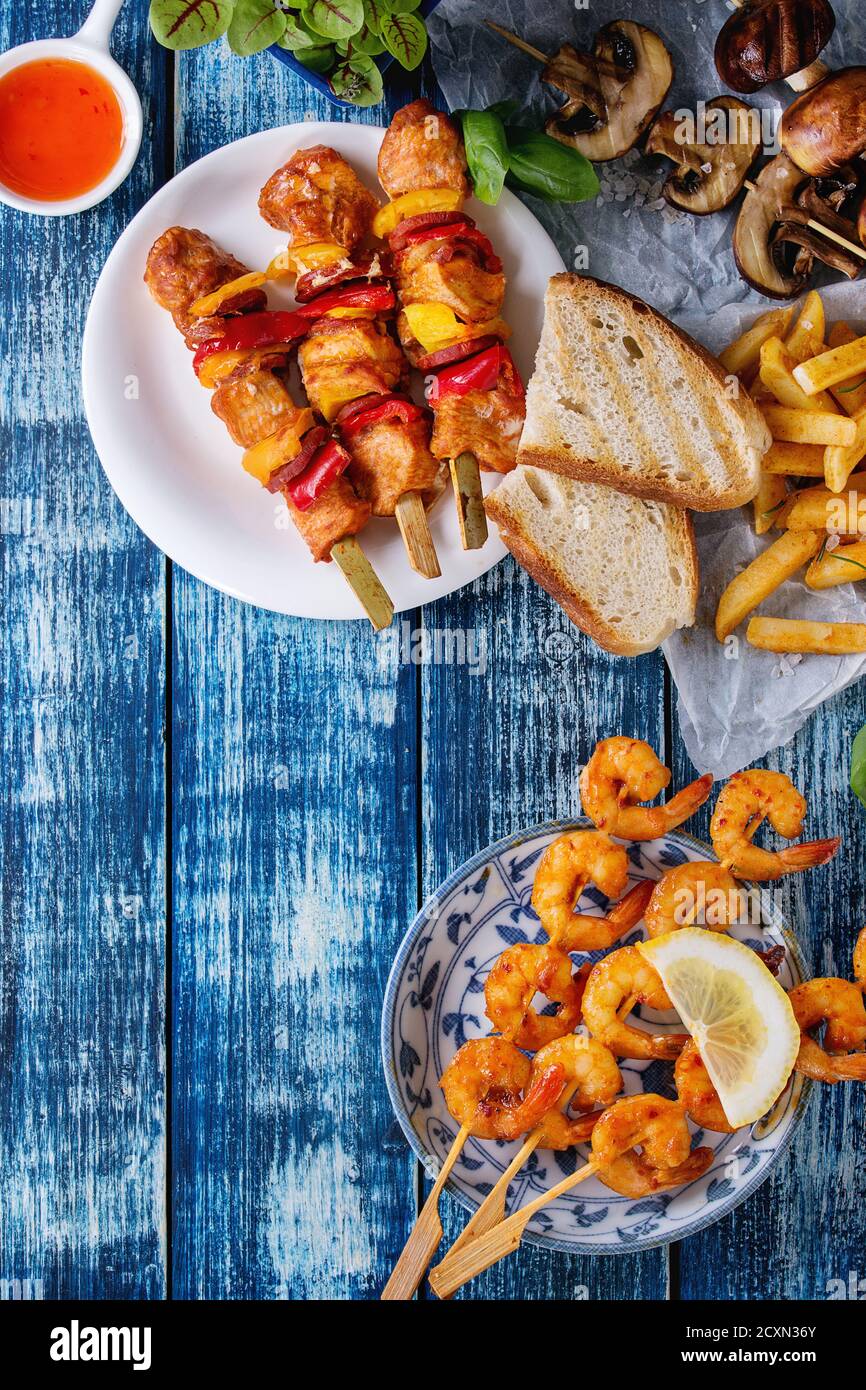 Varietà di snack barbecue il pranzo. Lastre grigliate di piccante spiedini di gamberi, pollo, maiale, verdure e funghi spiedini, pane, patate fritte patate con salse Foto Stock