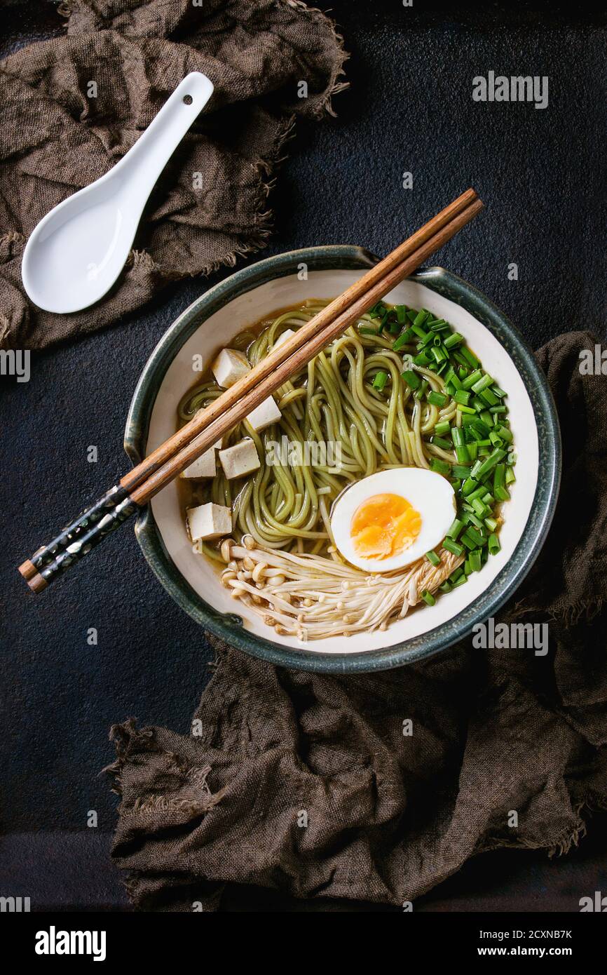 Ciotola di zuppa in stile asiatico con noodle di soba di tè verde, uova, funghi, cipolla e formaggio tofu, servita con bastoncini e cucchiaio bianco su sackcoot Foto Stock