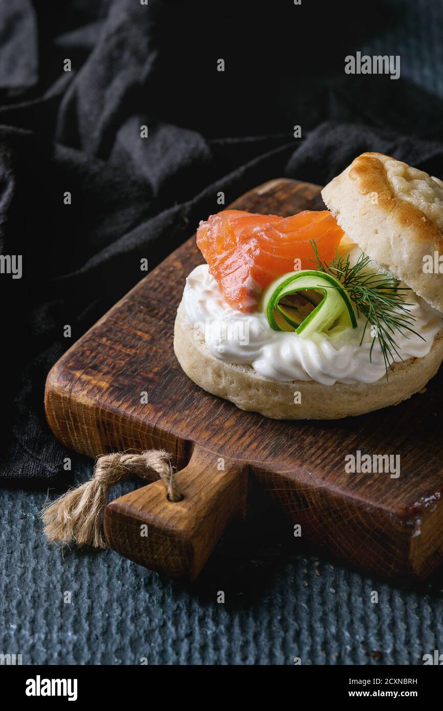 Focaccine di formaggio inglese tradizionali tagliate a fette con salmone affumicato, formaggio cremoso e cetriolo fresco serviti su tagliere di legno su backgr di tessitura nera Foto Stock