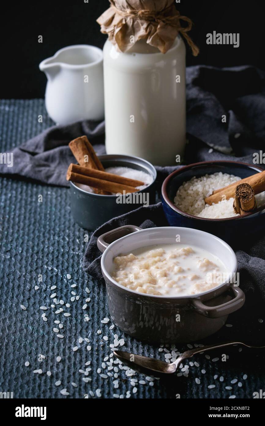 Ingredienti per rendere budino di riso. Ciotola di bianco il riso crudo, zucchero, bastoncini di cannella, bottiglia di latte e la brocca di crema e la pentola di cottura o budino Foto Stock
