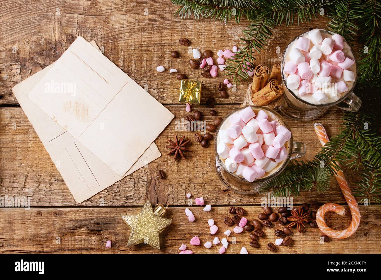 Due bicchieri di caffè latte con marshmallow rosa con biglietto d'auguri vuoto, decorazioni natalizie, zucchero rosa, caramelle, spezie, chicchi di caffè e abete rosso Foto Stock